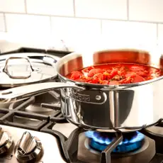 All-Clad D3 3-quart stainless steel saucepan filled with simmering tomato sauce over an open gas stove flame.