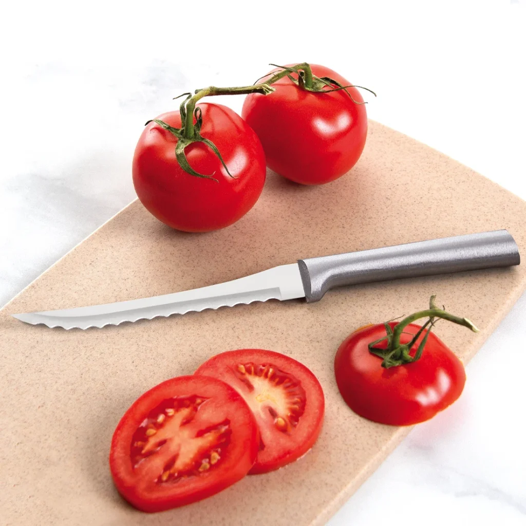 Rada Cutlery Tomato Slicer knife lying beside sliced and whole red vine tomatoes on a tan cutting board.